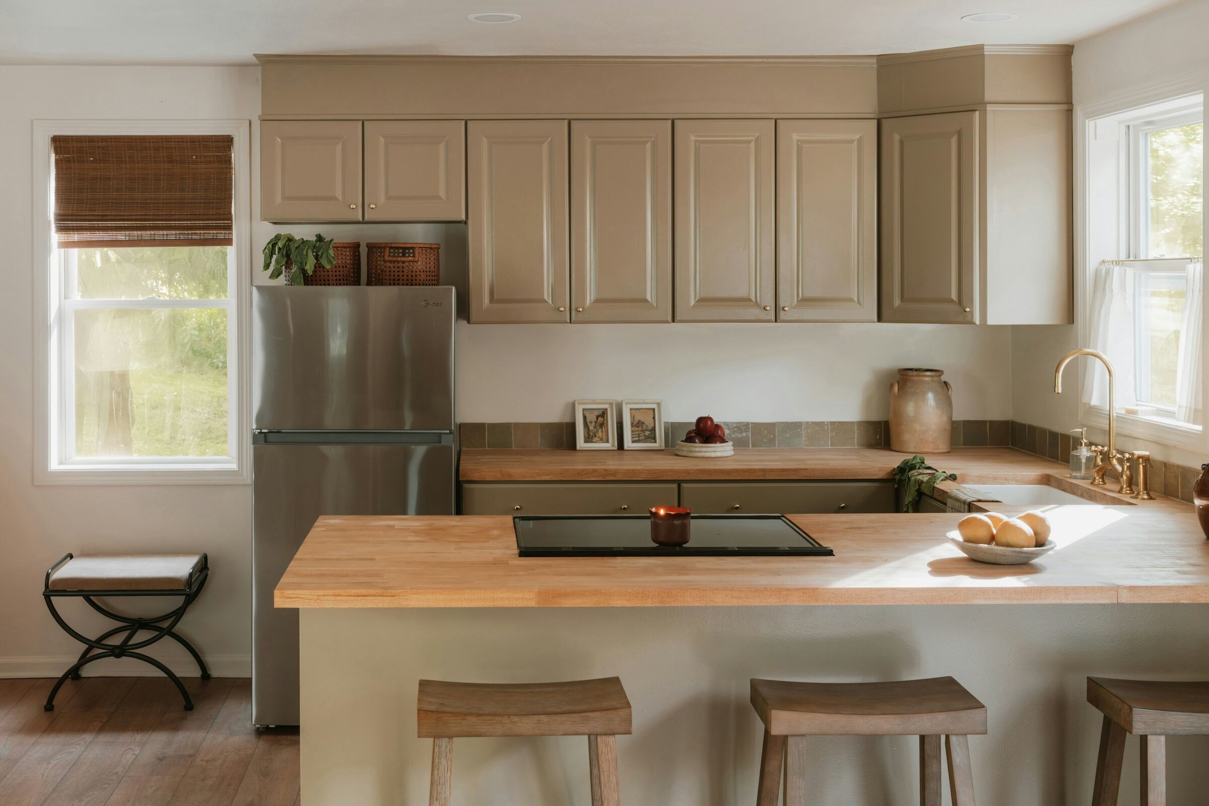 Cuisine lumineuse avec plan de travail en bois, placards beige et tabourets